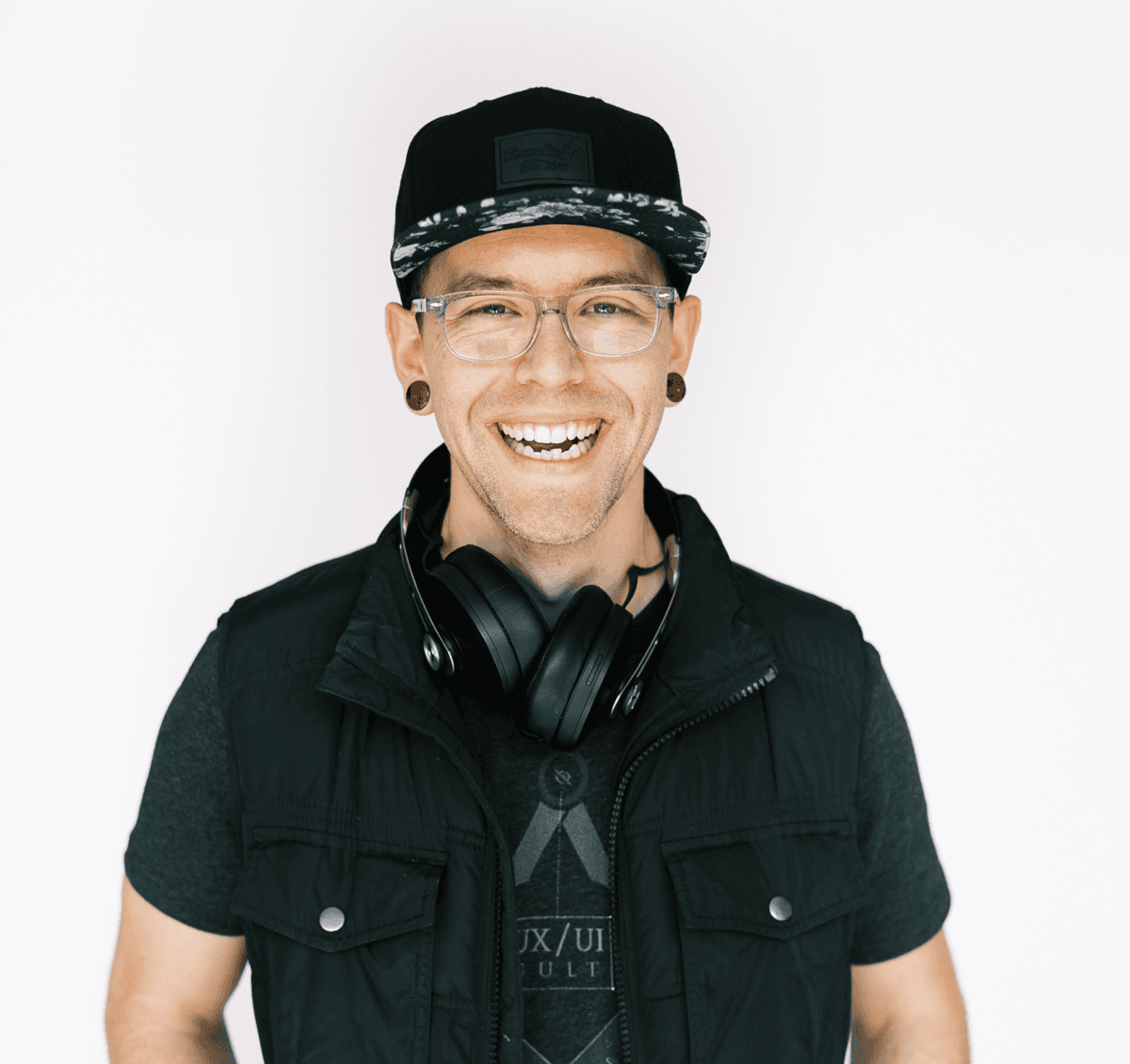 Zac Elletson — portrait, smiling, in a black snapback and vest with headphones around the neck